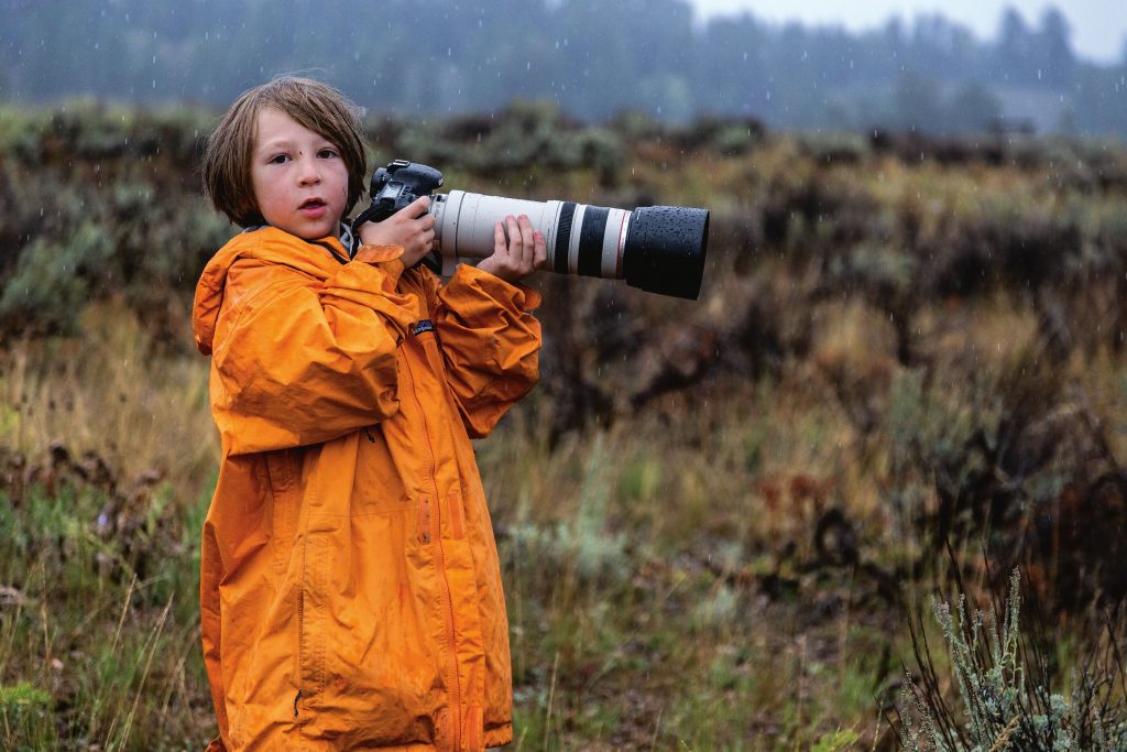 Patagonia boy in adult jacket holding huge camera