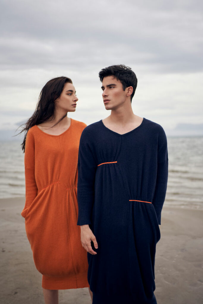 Two people wearing handknitted cashmere dresses, one orange and one navy